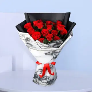 A bouquet of red roses wrapped in white and black marble-patterned paper tied with a red ribbon.