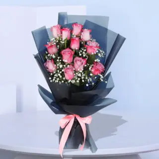 Bouquet of 12 purple roses with gypsophila in a black wrap, tied with a light pink ribbon.