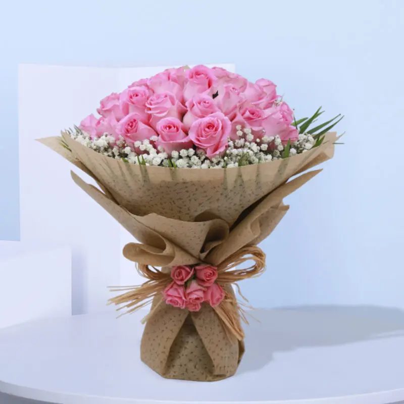 1 (81) A bouquet of pink roses with baby's breath wrapped in brown paper and tied with a natural coir.