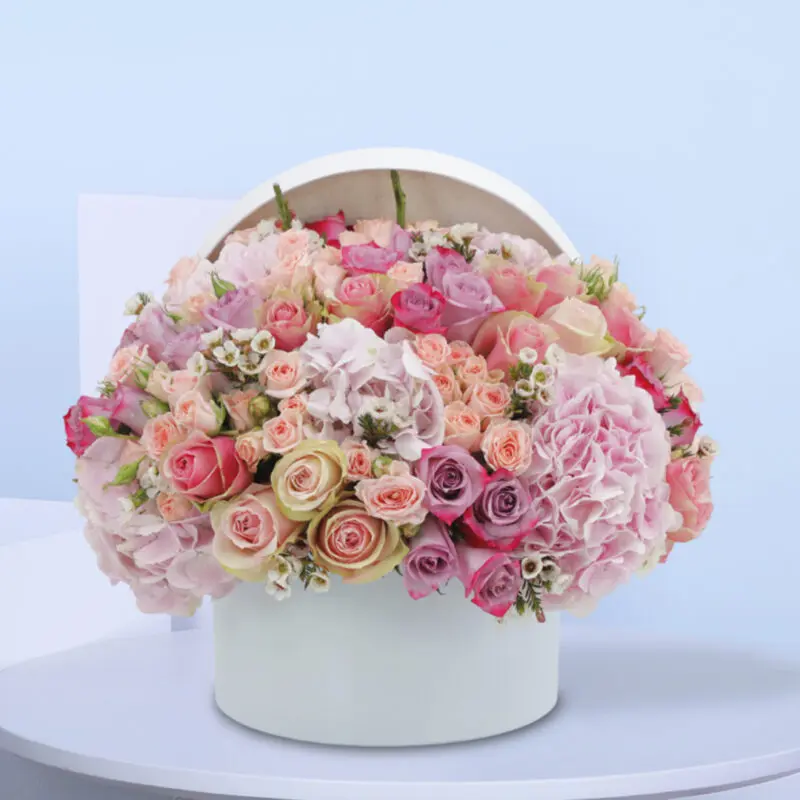 A white box filled with pink roses, carnations, and other pink flowers
