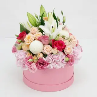 A pink hat box filled with a colorful arrangement of roses, lilies, ping pong chrysanthemums, and other flowers.