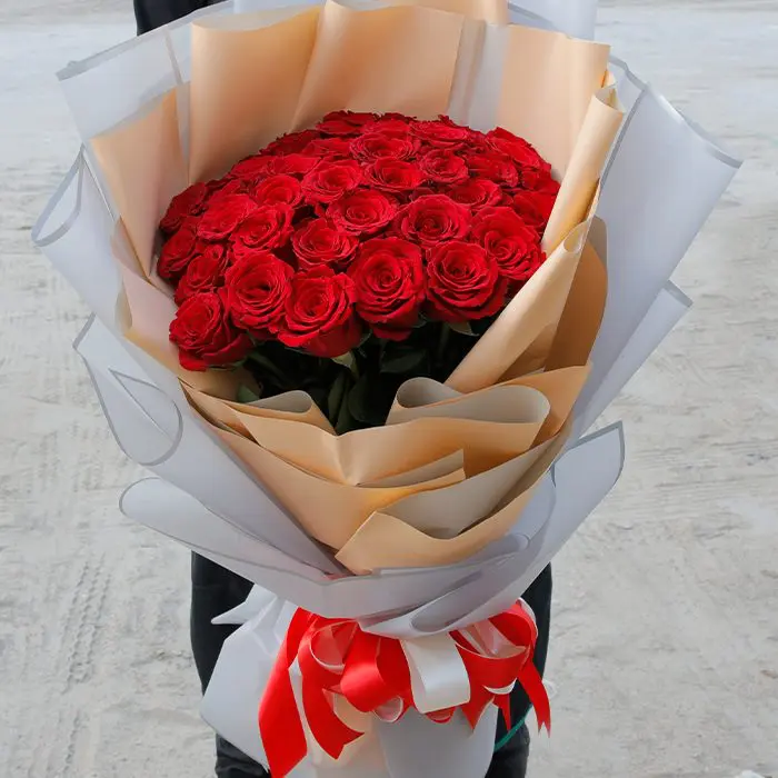 hand_bouquet_of_appealing_roses.png 50 stems of red roses arranged in a peach and white wrap, tied with a red ribbon.