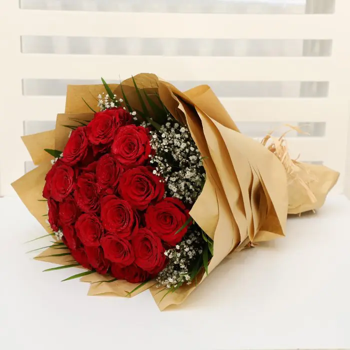 hand_bouquet_of_bewitching_red_roses.png A stunning bouquet featuring vibrant red roses, delicate gypsophila, and lush greenery, beautifully arranged and wrapped in natural brown paper.