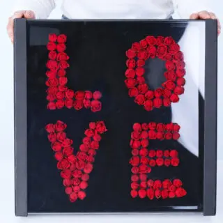 Spray roses arranged to spell "LOVE" inside a clear square box, creating an elegant floral display.