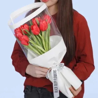 A bouquet of 10 red tulips wrapped in a white transparent cover, elegantly tied with a white bow.
