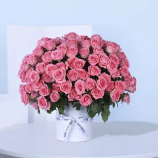 A white circular box filled with light pink roses, arranged in a circular pattern tied with white ribbon.