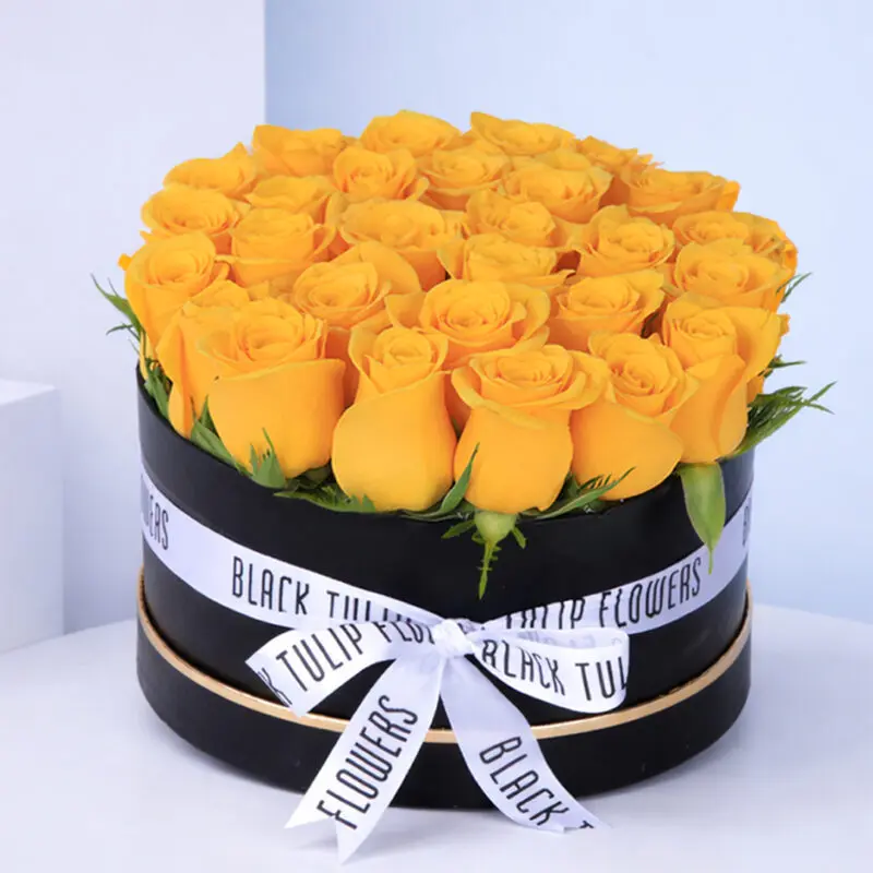 A black box filled with bright yellow roses, tied with a white ribbon.