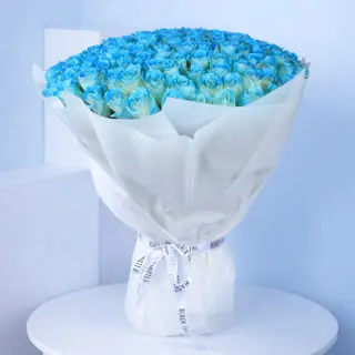 Elegant bouquet of 100 spray-painted blue roses in a white wrap tied with white ribbon.