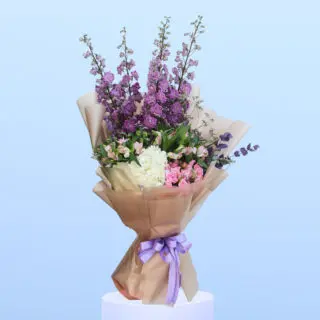 Mixed flowers beautifully arranged in a light brown wrap, elegantly tied with a lavender shade ribbon.