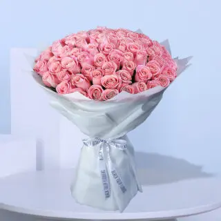 A large bouquet of light pink roses wrapped in white paper with white ribbons.