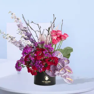 Bold and contemporary flower arrangement of pink roses, purple delphinium, and anthurium in a black box.