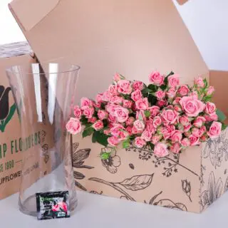 A bunch of spray roses in a glass vase, accompanied by flower food for added freshness and longevity.