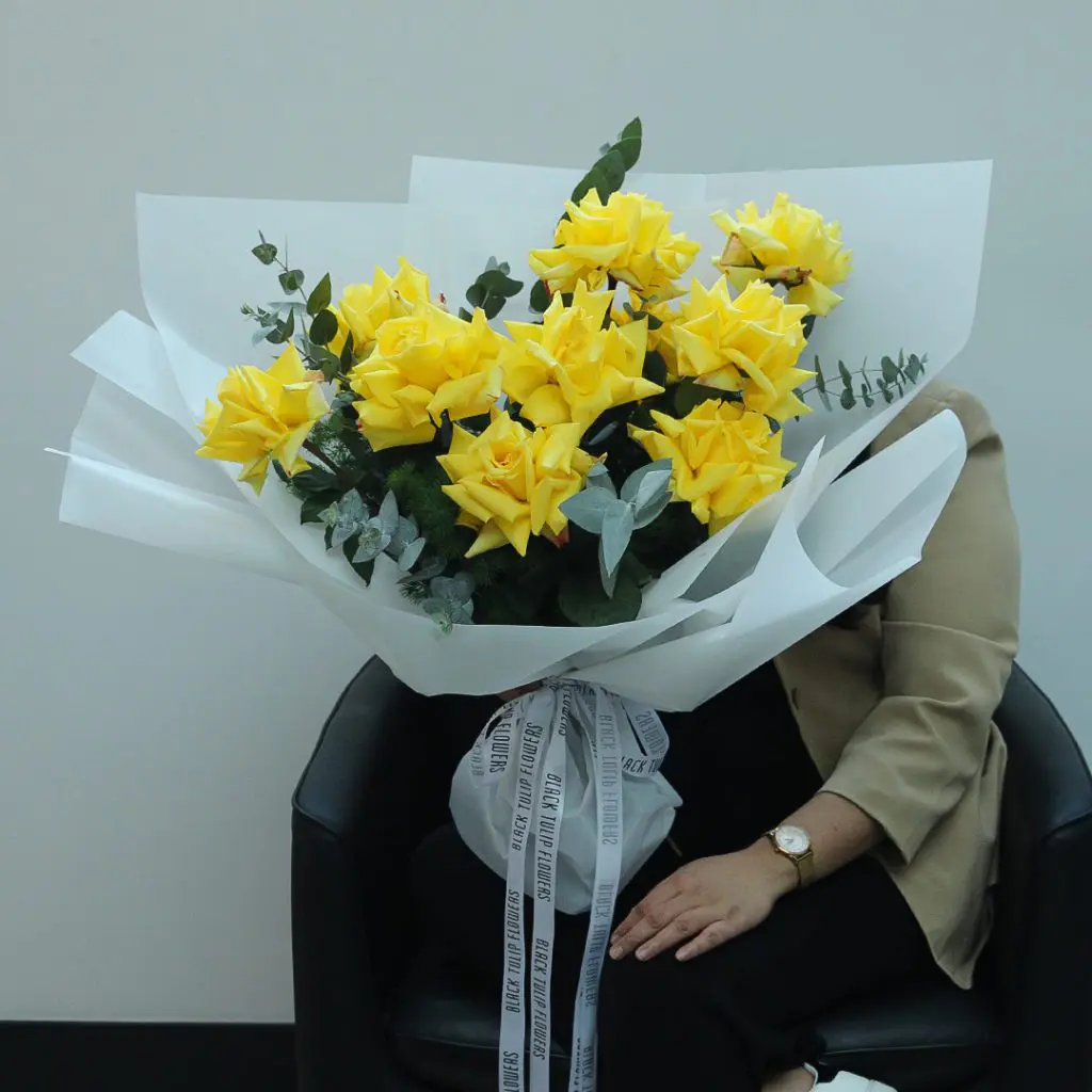 1927 A large bouquet of bright yellow roses wrapped in white paper with green eucalyptus leaves.