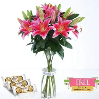 A bunch of pink lilies in a glass vase, accompanied by a box of Ferrero Rocher chocolates.