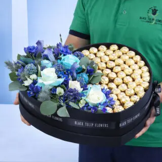 A black heart-shaped box filled with blue flowers and a large number of Ferrero Rocher chocolates.