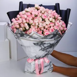 50 stems of pink spray roses arranged in a marble wrap and tied with a pink ribbon.