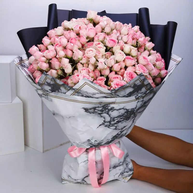 Charming Beauty (1) 50 stems of pink spray roses arranged in a marble wrap and tied with a pink ribbon.