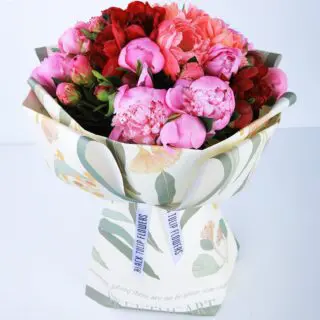 A bouquet of mixed peonies - pink and red wrapped in floral patterned paper.