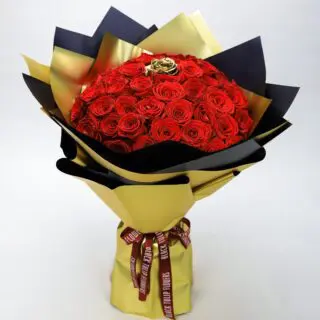 A bouquet of 49 red roses with one spray-painted golden rose in the center, wrapped in gold paper tied with a maroon ribbon.