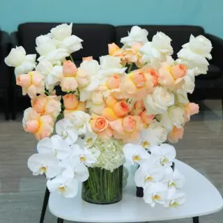 Stunning floral display of white and peach roses, orchids, and hydrangeas in a glass vase.