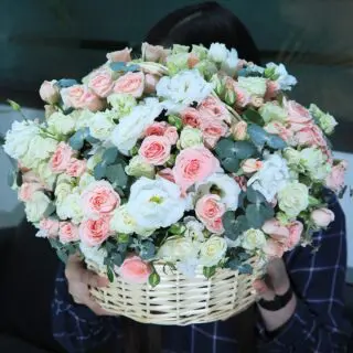 A large wicker basket filled with pink, white roses and eucalyptus.