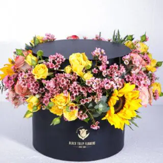 A circular black box filled with a colorful arrangement of sunflowers, roses, and other flowers.