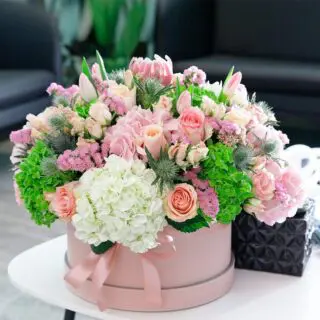 A beautiful arrangement of fresh flowers in a pink box adorned with a pink ribbon, showcasing a lovely mix of colours and blooms.