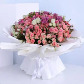 A bouquet of assorted pastel roses in a white wrap tied with a white ribbon.