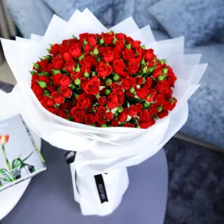 A bouquet of 50 stems of spray roses wrapped in white and tied with a black ribbon.