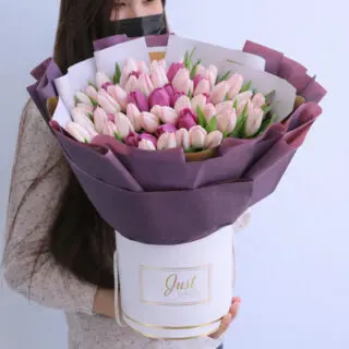 Light pink and purple tulips bouquet in purple wrap in a striped pink and white easy-to-carry box, tied with a white ribbon.