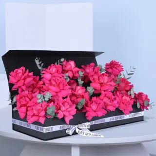 A rectangular black box filled with 28-30 pink roses and eucalyptus, beautifully tied with a white ribbon.