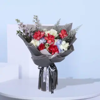 A stunning hand bouquet featuring roses, hydrangeas, delphinium, and seasonal fillers, wrapped in grey and tied with a black and white ribbon.