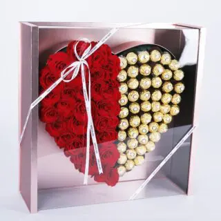 A heart-shaped gift box with a transparent lid, featuring red roses on one side and Ferrero on the other, tied with a red ribbon.