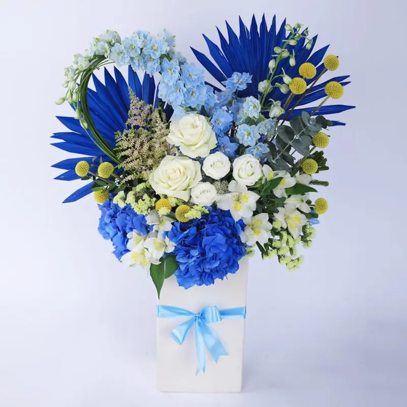 A charming white box filled with blue and white blooms, elegantly tied with a blue ribbon.