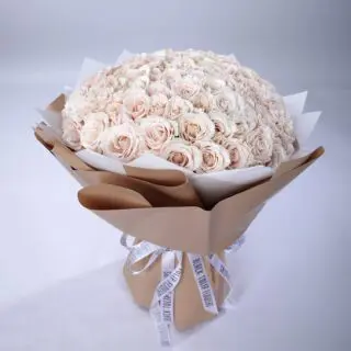 Luxurious bouquet of 100 creamy white roses wrapped in brown paper tied with white ribbon.