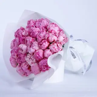 A large bouquet of pink peonies wrapped in white paper, sitting in a white box