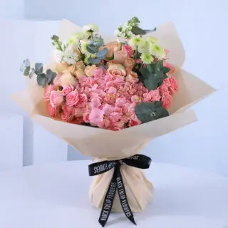 A bouquet of pink and peach flowers wrapped in beige paper with a black ribbon.