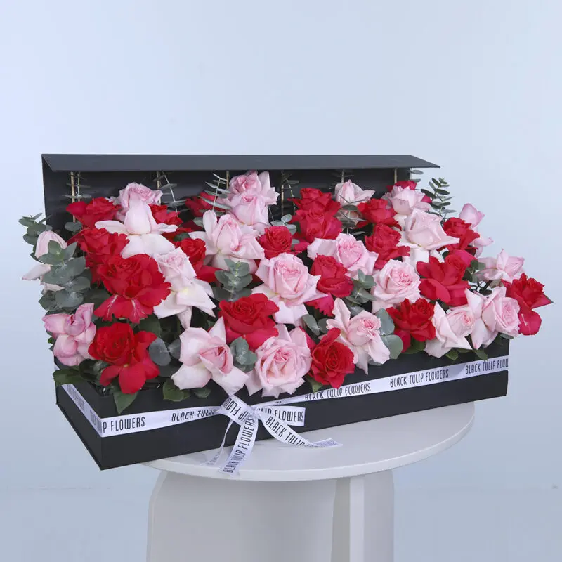 A stunning arrangement of Ohara and red roses, accented with eucalyptus leaves, in a rectangular black box tied with a white ribbon.