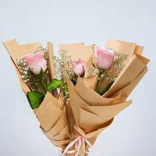 A bouquet of pink roses wrapped in brown paper.