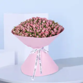 A large bouquet of 100 pink spray roses wrapped in pink paper with a white ribbon.