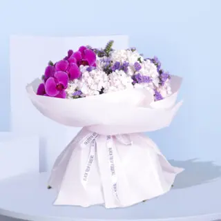 Pink orchids and purple hydrangeas, wrapped in white paper with a pink ribbon