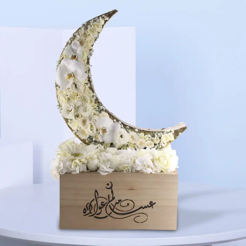 Ramadan Kareem - White Themed Crescent (1) A floral arrangement shaped like a crescent moon, made of white flowers, in a light wooden box with Arabic calligraphy