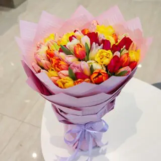A large bouquet of mixed color tulips wrapped in pink paper.
