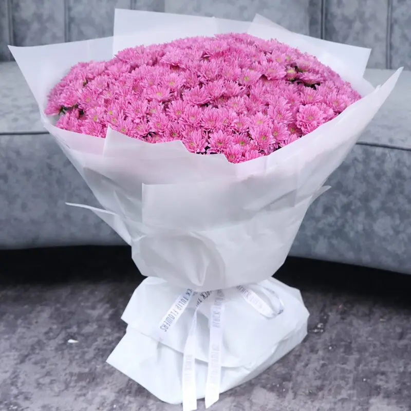 large bouquet of pink chrysanthemums wrapped in white paper.