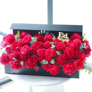 A black box filled with dark pink peonies and greenery. The lid of the box has "Eid Mubarak" written on it in gold.