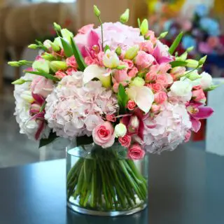 colorful bunch of of various flowers, including roses, hydrangeas, and lilies, arranged in a glass vase.