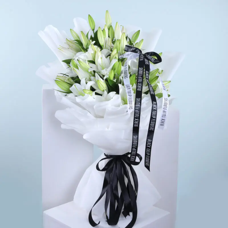 Casablanca White Lilies A large bouquet of pristine white lilies, elegantly wrapped in white tissue paper and tied with a black ribbon.