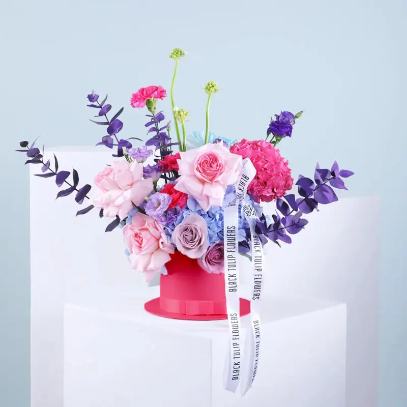 Images (1) A mix of blue and pink hydrangeas, roses, lisianthus, carnations, ornithogalum, and chrysanthemum with eucalyptus in a pink hatbox tied with a white ribbon.