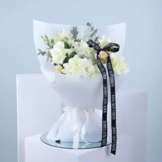 Bouquet of white and peach flowers with eucalyptus in a white wrap tied with a white ribbon and accompanied by a black ribbon.