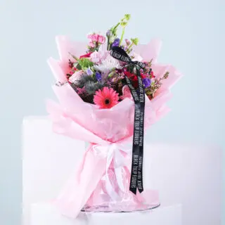 A colorful mixed flower bouquet wrapped in pink tissue paper and tied with a black ribbon featuring the Black Tulip Flowers